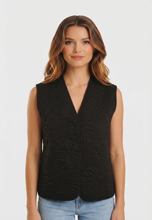 Femme aux cheveux bruns ondulés portant un gilet sans manches noir texturé et un jean bleu clair, face à l'avant sur un fond blanc.