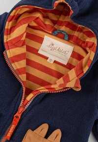 Giacca in pile blu marino con una fodera a righe arancioni e gialle, dotata di chiusura zip e tasca a forma di zampe di animale.