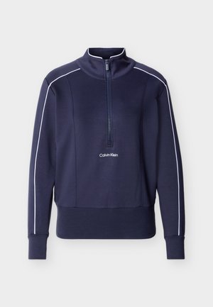 Tumši zils garroku pulovers ar baltu apmali uz piedurknēm, pusritentiņu priekšpusē, imitācijas apkakli un "Calvin Klein" logo uz krūtīm.