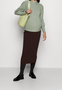 Jasnozielony sweter z prążkowanym wzorem i bufiastymi rękawami, zestawiony z brązową prążkowaną spódnicą midi. Czarne mokasyny i wpleciona torba w zielono-żółte wzory.