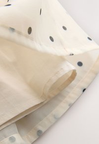 Tissu crème à pois noirs présentant des détails pliés et cousus sur un textile léger et transparent.