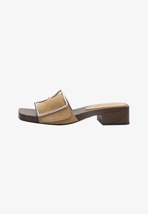 Sandalo aperto in suede marrone con punta aperta, ampia fascia, grande fibbia d'argento e tacco basso a blocco in legno su sfondo bianco.
