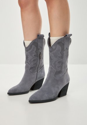 Botas de cowboy de ante gris con punta afilada, cortes decorativos y tacón cuadrado. Cuentan con un zipper lateral para facilitar su uso.