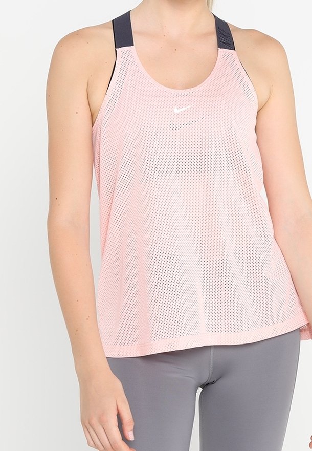 Femme portant un débardeur en mesh rose avec des bretelles noires et un legging gris, debout devant un fond uni.