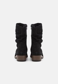 Botas de tobillo de ante negro con un diseño arrugado, cremalleras laterales y un tacón apilado marrón. Presentan un detallado pespunte a lo largo de las costuras.