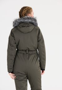 Olivgrön isolerad overall med knytmidja, utrustad med en avtagbar grå fuskpälsfoder huva och långa ärmar. Slät textur.
