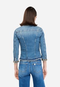 Jeans jakna z oprijetim krojem, skrajšano dolžino, raztrganim robom in verižnimi poudarki na rokavih. Svetlo modra barva in klasični zadnji šivi.