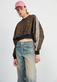 Hu leopard print cropped sweatshirt met zwarte boorden en drie witte strepen; lichtblauwe jeans met oranje zijstreep en logo op de zak.