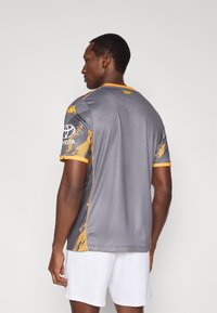 Szürke sportmez rövid ujjal, sárga részletekkel a galléron és az ujjakon, texturált mintával és logóval a bal vállnál.