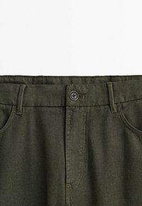 Oliivinvihreät housut, joissa on teksturoitu kangas, edessä nappikiinnitys, vyölenkit ja sivutaskut. Yksinkertainen, toiminnallinen muotoilu.