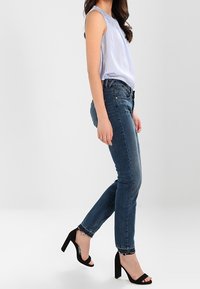 Haut sans manches bleu clair avec un motif texturé, associé à un jean skinny bleu foncé. Sandales à talons carrés noires.
