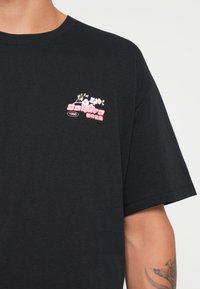 Black cotton t-shirt featuring a small embroidered design with pink text and white flower accents on the left chest area.