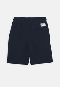 Tummansinisiä puuvillahousuja, joissa on joustava vyötärö, takatasku ja pieni logo-etiketti. Sujuva rakenne ja rento muotoilu.