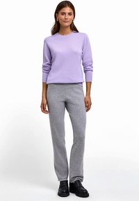 Hellvioletter Strickpullover mit rundem Ausschnitt und gerippten Bündchen, kombiniert mit grauer, weicher, zulaufender Hose. Schwarze Schuhe vervollständigen den Look.