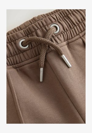Pantaloni de trening maro cu talie elastică, prevăzuți cu inele argintii și șnur împletit cu capete metalice. Material moale, texturat.