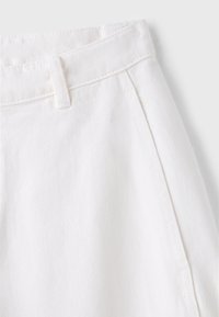 Gros plan d’un tissu denim blanc montrant la ceinture, la passants de ceinture, la couture latérale et le bord de la poche avec une couture visible.