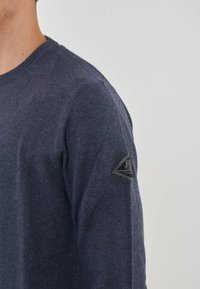 Maglione lavorato a maglia blu navy con scollo rotondo; presenta un tessuto testurizzato e una toppa a forma di triangolo sulla spalla sinistra.