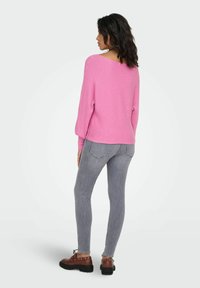 Rosa, ribbestrikket genser med bred hals, lange ermer og avslappet passform. Kombinert med grå skinny jeans og brune snørestøvler.