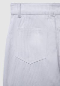 Weiße Cordhosen mit einer strukturierten Oberfläche, Seitennaht und einer einzelnen Gesäßtasche mit einer Raute nahe der Kante.