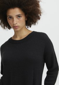 Schwarzer Strickpullover mit Rundhalsausschnitt und gerippten Bündchen. Weiche Textur und lockere Passform, mit gerippten Akzenten an den Schultern.