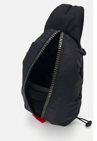 Sac noir avec une ouverture zippée, surface texturée, poche en mesh à l'intérieur et accents rouges. Présente un texte imprimé le long du zip.