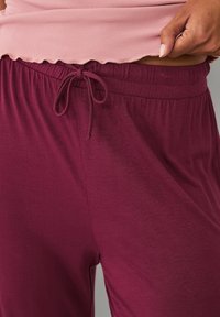 Maroon elastic-waist pants with a drawstring, soft texture, and relaxed fit. Layered with a pink ribbed top featuring a scalloped hem.