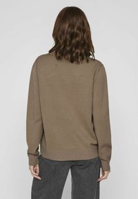 Suéter de punto marrón con un corte holgado, puños y dobladillo acanalados. Lleva puesto sobre pantalones gris oscuro, mostrando un diseño simple sin adornos.