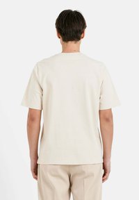 Camiseta de manga corta color beige hecha de algodón, con cuello redondo y un ajuste relajado. Diseño liso sin patrones ni logotipos visibles.