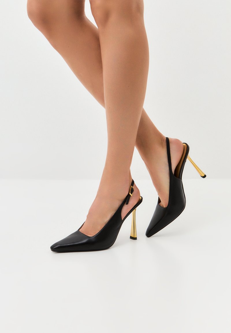 Cizme cu toc slingback din piele neagră, cu vârful ascuțit și toc stiletto metalic auriu. Design cu laturi deschise și curea de gleznă neagră cu cataramă.