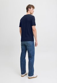 T-shirt di cotone blu navy con colletto tondo, abbinata a jeans denim blu e sneakers bianche basse. Design semplice, vestibilità standard.