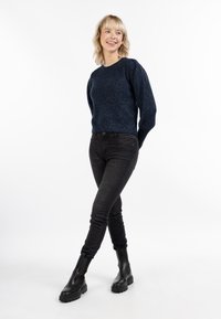 Hajós kötött pulóver texturált dizájnnal, kerek nyakkivágással és hosszú ujjakkal, fekete skinny farmernadrággal és fekete bokacsizmával párosítva.