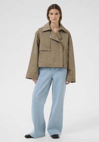 Khaki cropped jack met een brede kraag, dubbele knopen en een textuurstof, gecombineerd met lichtblauwe wijde jeans.
