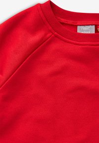 Punane dressipluus soonikkoelise ümara kaeluse ja raglaanvarrukatega. Sile tekstuur, minimaalne õmbluste detail, sildiga "next school."