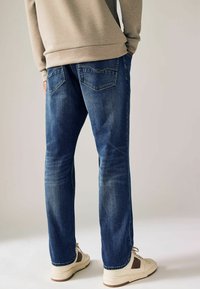 Blauwe denim jeans met een rechte pasvorm, vervaagde details en twee achterzakken, gecombineerd met crème en bruine sneakers.
