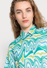 Camisa colorida com um padrão de ondas em verde, azul e branco, com gola e fecho de botão. Tecido suave.