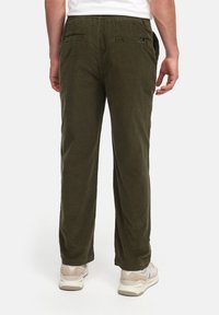 Los pantalones de pana verde oliva presentan un corte recto, cintura elástica y dos bolsillos traseros con cierres planos. La tela tiene un acabado texturizado.
