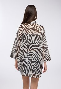 Camicia a strisce zebra traslucida con una forma rilassata, maniche lunghe e orlo spaccato. I colori includono nero e avorio.