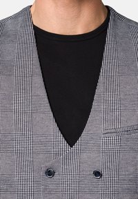 Czarna kamizelka w kratę, z głębokim dekoltem w kształcie litery V, podwójnymi guzikami i kieszenią z przodu. Materiał ma gładką fakturę.