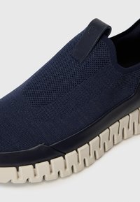 Navy slip-on sneaker with knitted upper, textured design, and contrasting chunky cream sole. Features a pull tab for easy wear.