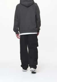 Mörkgrå huvtröja med en kenguruficka, kombinerad med löst sittande svarta cargobyxor med sidofickor. Vit underskjorta syns vid fållen.