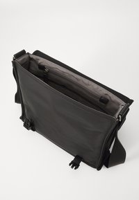Sac messager noir avec un extérieur en tissu lisse, une poche zippée à l'intérieur et une sangle réglable. Possède une forme rectangulaire élégante.