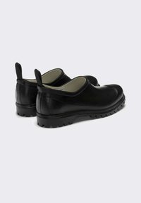 Un paio di scarpe in gomma nere slip-on con bretelle e suole robuste, angolate per mostrare i lati e il retro su uno sfondo semplice.