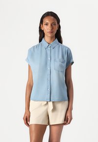 Lys blå denimskjorte med korte ermer og knappelukking foran. Har en enkelt brystlomme og en avslappet passform.
