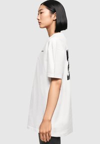 Hvid bomulds oversized t-shirt med korte ærmer, rund halsudskæring og sort tekstdesign på bagsiden. Glat tekstur, lige snit.