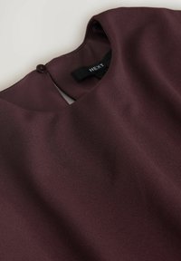 Burgundská blůza s hladkým povrchem, kulatým výstřihem a zapínáním na knoflíky na zadní straně. Obsahuje štítek s označením "NEXT."