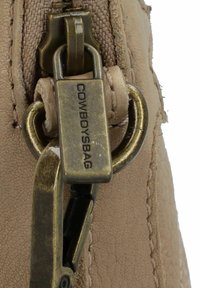 Tirante in pelle tan con etichetta incisa "COWBOYSBAG". Caratterizzato da accessori in ottone e una superficie testurizzata, che mette in risalto durabilità e design.
