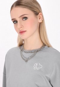 Szürke kapucnis pulóver hosszú ujjakkal, fehér hímzett szív és mancs mintával. Három rétegű ezüst láncnyakláncok. Simás textúra.