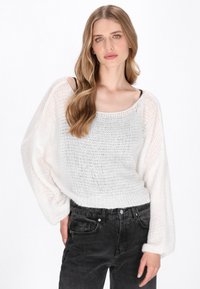 Biały, dzianinowy sweter o luźnym kroju i szerokich rękawach. Teksturowany wzór i prążkowany dół; zestawiony z czarnymi spodniami typu high-waist.