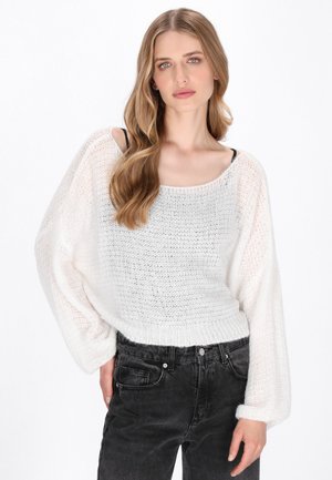 Maglione bianco a maglia con una vestibilità ampia e maniche larghe. Motivo testurizzato e orlo a coste; abbinato a jeans neri a vita alta.