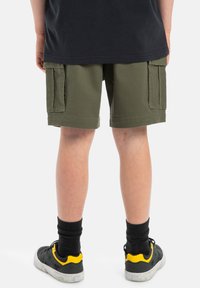 Olivgröna cargo-shorts med två sidofickor, bomullsmaterial, knälång, som är kombinerade med svarta strumpor och svarta/gula sneakers.